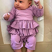 Elisa is registered to the contest to win money with this photo: baby, infant, child, purple_clothing, ruffles, cushion, lying_down, barefoot, cute, skin, face, hands, legs, feet, indoors, soft_fabric, closeup, newborn, expression, small_fingers