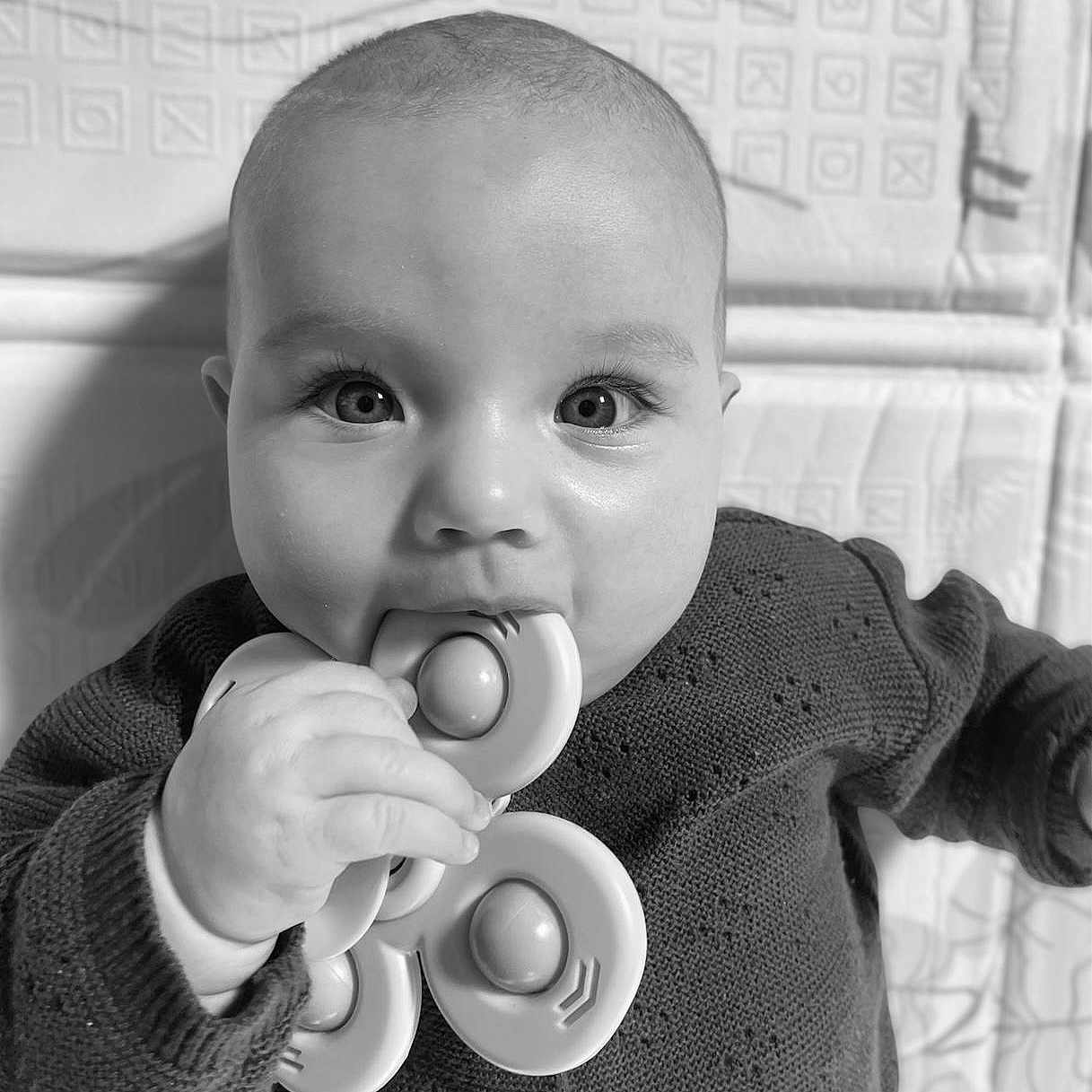Charlie participe au concours pour gagner de l'argent avec cette photo : baby, black_and_white, chewing, child, closeup, curious, cute, eyes, face, fidget_spinner, hand, indoor, infant, knitted_sweater, patterned_background, person, playful, portrait, toy, young