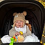 baby, child, stroller, hat, knitwear, plush_toy, autumn, outdoor, pavement, leaves, fall, cute, face, expression, warm_clothing, person, smile, sitting, bundle, toy