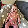 baby, child, smile, happy, infant, cushion, cloud_pattern, pink_clothing, sitting, indoor, sofa, cute, joyful, person, face, home, comfort, plush, cozy, casual