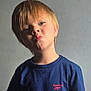 blond_hair, blue_tshirt, boy, casual_clothing, child, cute, expression, fashion, head_and_shoulders, human, indoor, person, plain_background, playful, portrait, pouting, short_sleeves, smile, studio_lighting, young