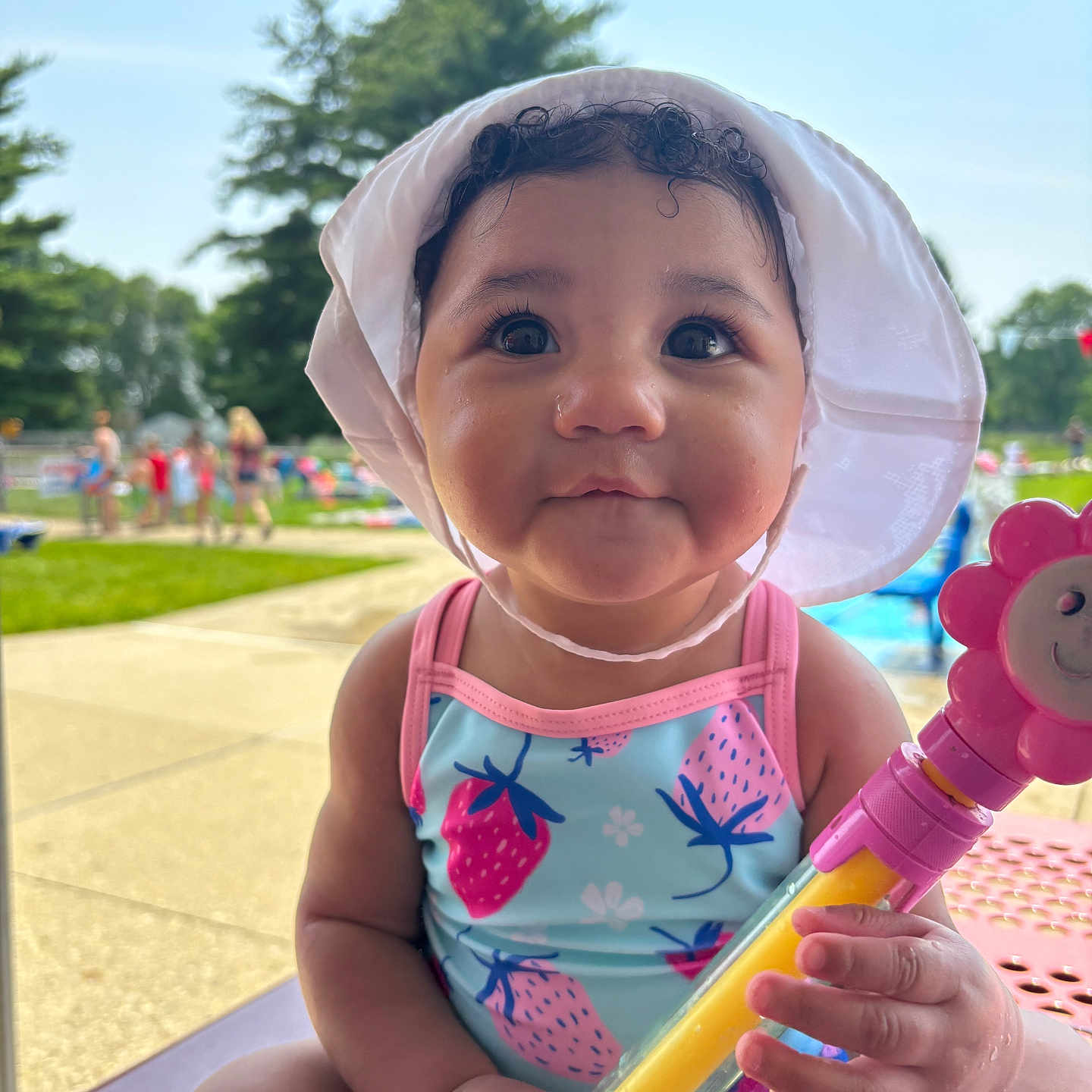 Alani joined the competition — help win amazing prizes! baby, bench, blue, child, cute, face, flower, grass, hat, outdoor, person, pink, playground, smiling, summer, sunhat, swimsuit, toy, tree, water