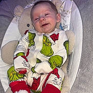 Ralphie is registered to the contest to win money with this photo: baby, infant, smiling, pajamas, grinch, red_booties, plush_toy, baby_seat, hanging_toys, heart_doodle, cozy, indoor, cute, child, clothing, comfort, portrait, holiday, soft_fabric, sleepwear