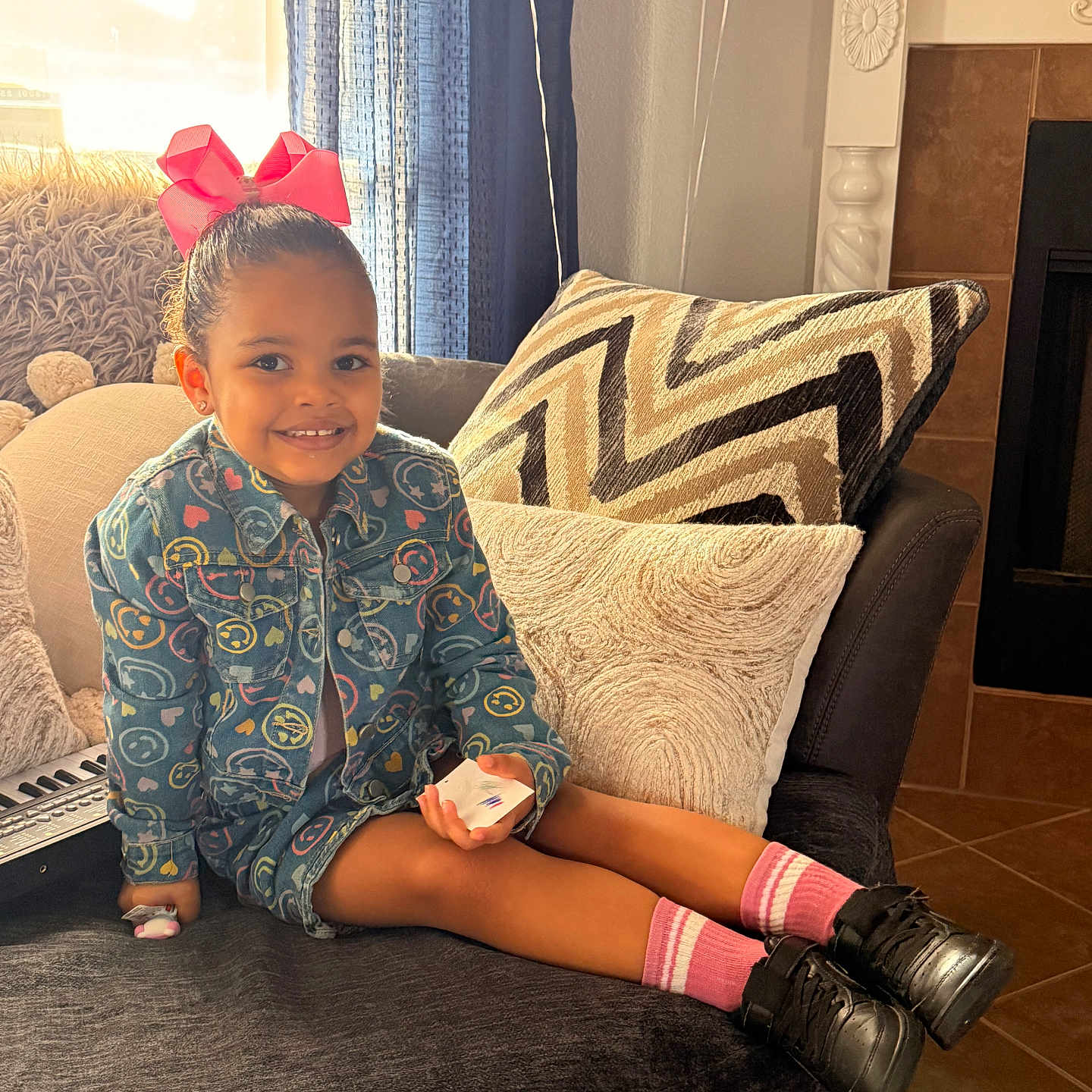 Eliana joined the competition — help win amazing prizes! balloons, black_shoes, child, couch, curtain, denim_jacket, fireplace, girl, hair_bun, keyboard, legs, living_room, patterned_jacket, pink_bow, pink_socks, plush_toy, sitting, smiling, throw_pillow, toy