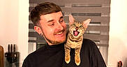 Luna is registered to the contest to win money with this photo: black_shirt, cat, countertop, cute, domestic_animal, earrings, expression, happy, indoor, kitchen, kitten, man, pet, portrait, short_hair, shoulder, smile, tabby_cat, utensils, window_blinds