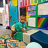 baby, balloon, child, classroom, colorful, crawling, face, indoor, padded_equipment, pencils, playground, playroom, portrait, road_map, rug, smiling, soft_play, standing, toddler, wall_decor