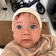 Ilyan a rejoint le concours — aidez-le/la à gagner de superbes lots ! baby, child, face, hat, sweater, indoor, blue_eyes, curious, closeup, portrait, infant, hands, expression, skin, headwear, person, floor, bicycle, background, tile_floor
