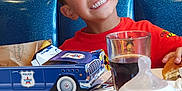 Milan Andrea a rejoint le concours — aidez-le/la à gagner de superbes lots ! baby_bottle, blue_booth, boy, bread, child, dining, food, fork, glass, happy, indoor, kid, pink_wall, playful, police_car, red_shirt, smile, soda, table, toy
