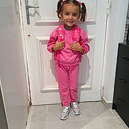 Valentina a rejoint le concours — aidez-le/la à gagner de superbes lots ! child, girl, pink_clothing, backpack, pigtails, smile, door, white_door, indoor, tile_floor, sneakers, silver_shoes, standing, happy, person, hair_ties, casual_wear, young_child, portrait, home_interior