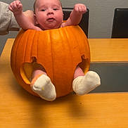 Theodore is registered to the contest to win money with this photo: baby, pumpkin, table, sock, hand, orange, face, child, holiday, autumn, cute, indoor, celebration, person, furniture, chair, smile, skin, holiday_decoration, festive