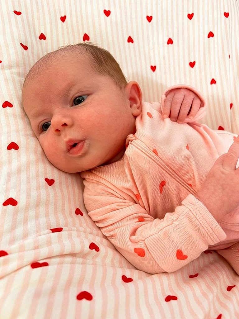 Isla is registered to the contest to win money with this photo: baby, infant, newborn, onesie, pink, hearts_pattern, bedding, blanket, crib, cute, adorable, face, eyes, hand, portrait, closeup, lying_down, soft, sleepwear, nursery