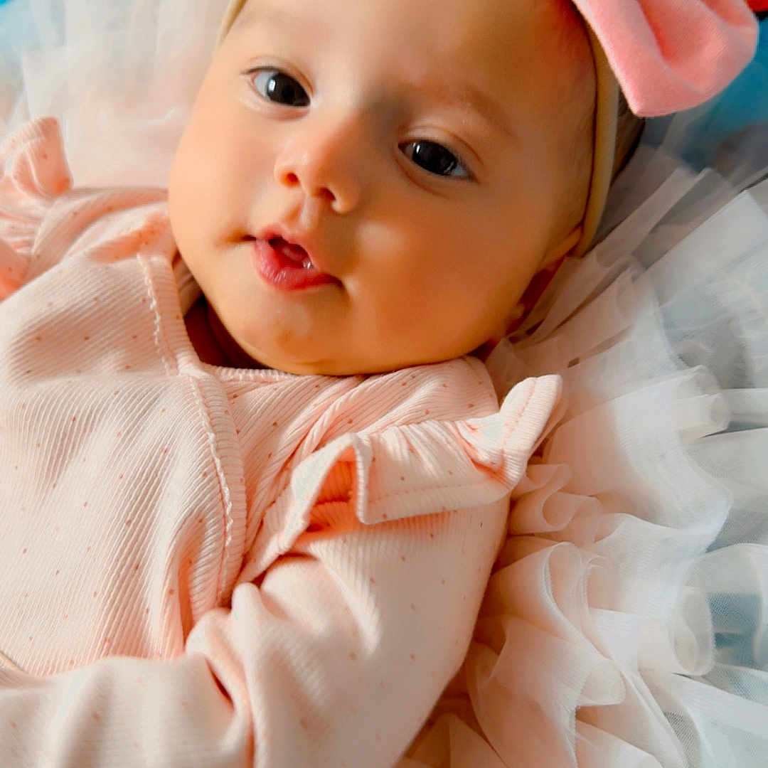 Zaynah joined the competition — help win amazing prizes! adorable, baby, blanket, bow, child, close_up, colorful_background, cute, face, happy, headband, indoors, infant, lying_down, newborn, peaceful, pink_clothing, portrait, ruffles, soft_fabric