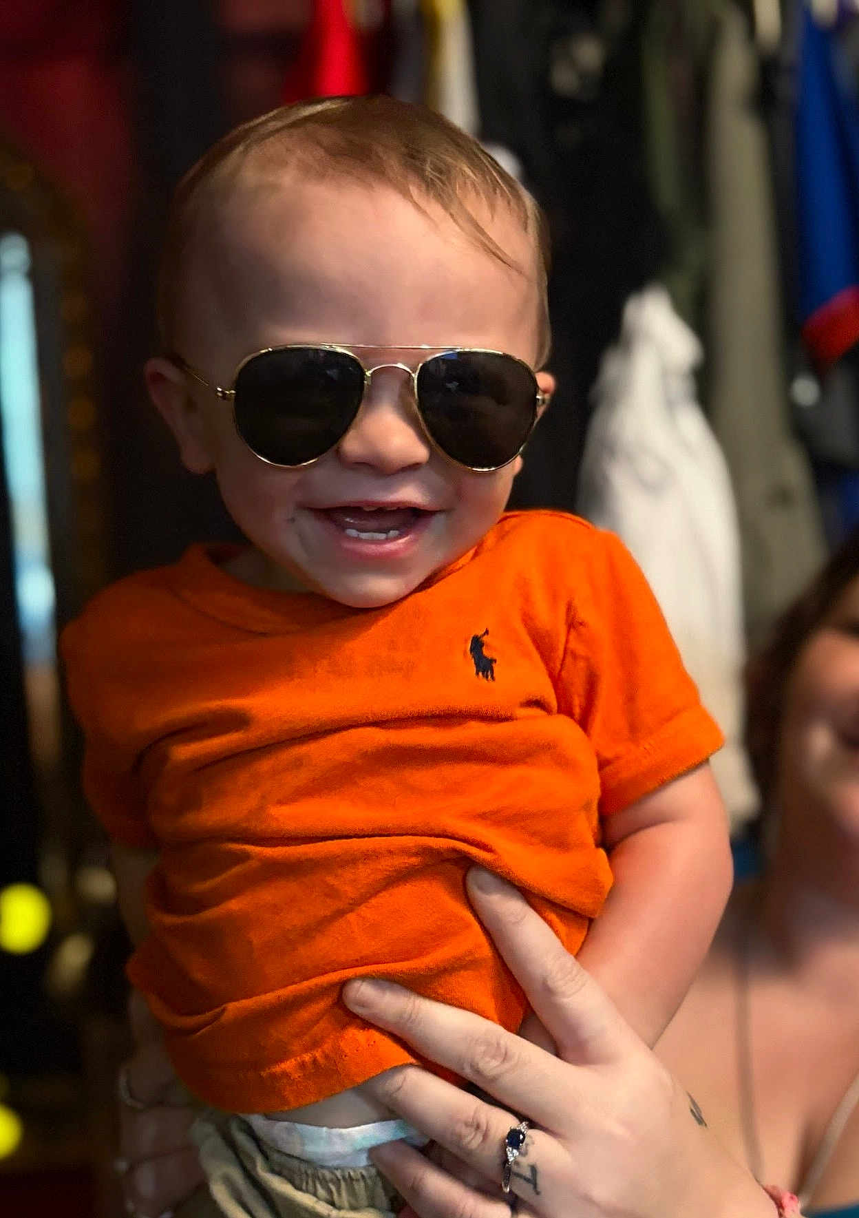 Brayden is registered to the contest to win money with this photo: toddler, child, sunglasses, orange_shirt, smile, happy, person, hand, indoor, clothing, face, portrait, cute, baby, fashion, accessory, holding, ring, tattoo, fun