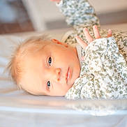 Maddi is registered to the contest to win money with this photo: baby, infant, face, blue_eyes, hand, floral_clothing, onesie, lying_down, soft_surface, skin, newborn, portrait, cute, child, young, peaceful, indoors, light, expression, sleepwear