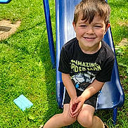 Axiss is registered to the contest to win money with this photo: child, boy, smiling, slide, playground, outdoor, grass, sunlight, casual_clothing, shorts, shoes, black_tshirt, toy, happy, summer, play, young, fun, nature, recreation
