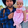 Lesly is registered to the contest to win money with this photo: man, baby, child, cowboy_hat, pink_dress, headband, outdoor, daylight, portrait, smile, beard, jeans, belt, backpack, person, sky, trees, palm_trees, holding, family