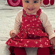 Lesly is registered to the contest to win money with this photo: baby, child, smiling, red_dress, white_shoes, leggings, bed, pillow, decorative_pillow, donut_pillow, cherry_pillow, indoor, cute, happy, portrait, infant, sitting, clothing, face, person