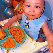 Braylen joined the competition — help win amazing prizes! baby, child, high_chair, eating, food, pasta, mashed_food, bib, blue_bib, smiling, face, portrait, indoor, birthday, balloons, party, colorful, table, messy_mealtime, seated