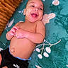 baby, infant, child, laughing, smiling, portrait, lying_down, blanket, floral_pattern, cushion, bed, indoor, bare_chest, black_shorts, sporty_clothing, happy, face, hands, cozy, photography