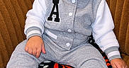 Braylen is registered to the contest to win money with this photo: baby, child, infant, portrait, sitting, armchair, couch, sneakers, shoes, outfit, jacket, gray_clothing, white_sleeves, toy, stuffed_animal, stacking_rings, indoor, home, colorful_background, fashion