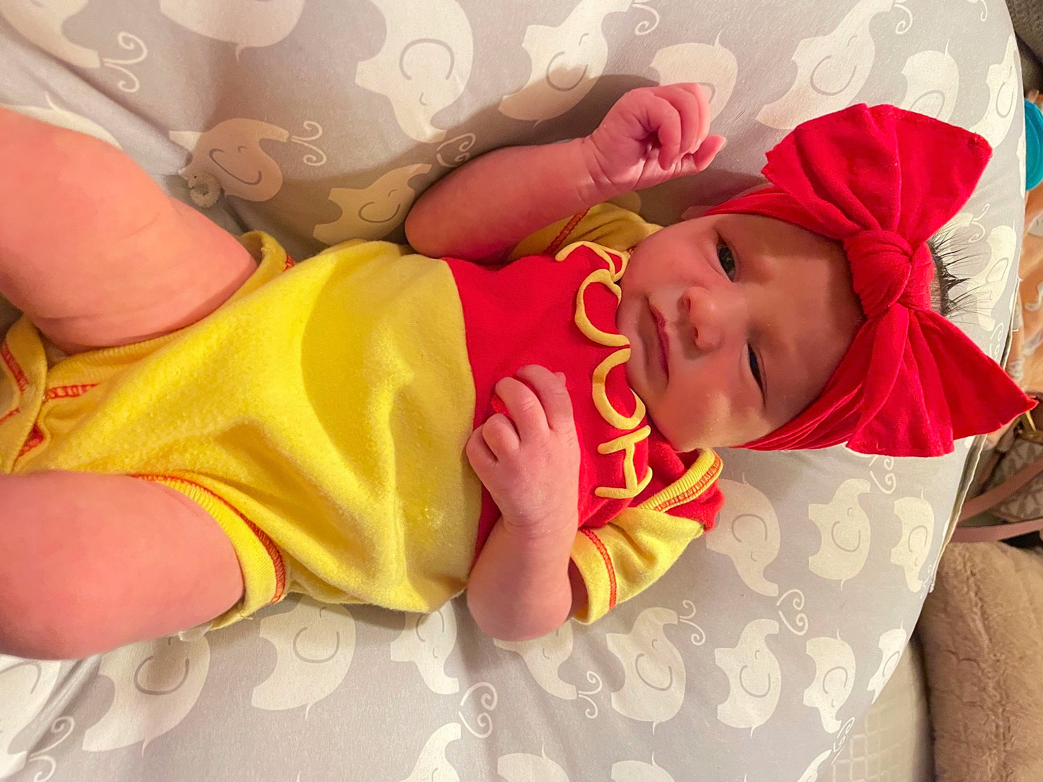 Kinsley is registered to the contest to win money with this photo: baby, baby_toddler_clothing, child, comfort, eye, finger, gesture, hand, happy, hat, headwear, human_leg, mouth, nail, orange, pattern, person, pink, skin, sleeve