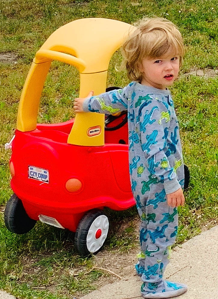 Dylan is registered to the contest to win money with this photo: automotive_tire, baby_toddler_clothing, child, face, fun, grass, happy, leisure, motor_vehicle, people_in_nature, person, photograph, recreation, riding_toy, sleeve, summer, t_shirt, tire, toddler, vehicle