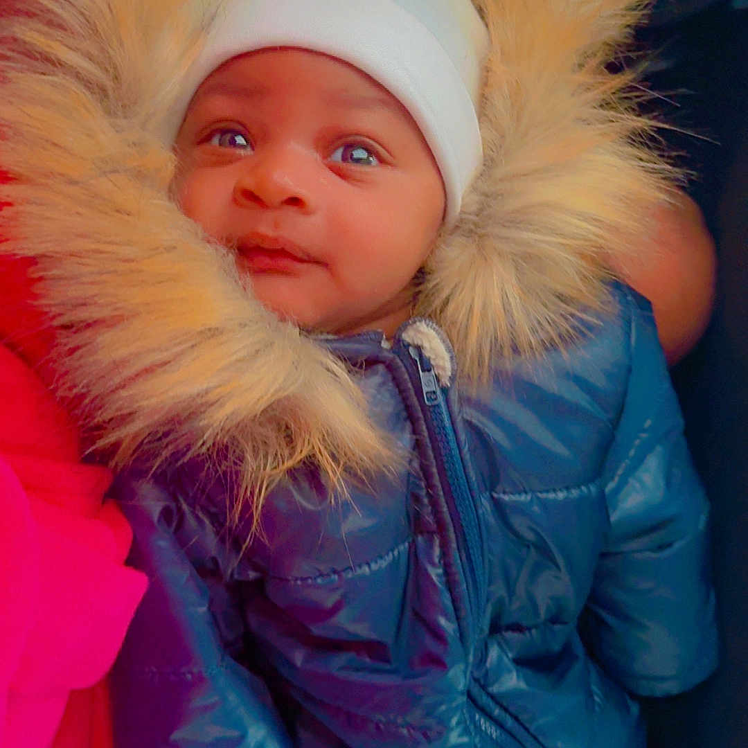 Jamaine joined the competition — help win amazing prizes! adorable, baby, blue, child, cute, face, fur_trim, gloves, hood, indoor, infant, looking_up, person, portrait, puffy_jacket, small, snowsuit, warm, white_hat, winter_clothing