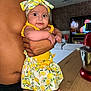 baby, child, person, shirtless, headband, lemon_pattern, yellow_clothing, arm, hand, kitchen, mixer, wooden_counter, television, living_room, brick_wall, couch, foot, table, indoor, holding