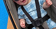 Walker joined the competition — help win amazing prizes! baby, child, infant, stroller, sunglasses, smiling, happy, portrait, outdoor, seated, harness, seatbelt, blue_clothing, patterned_clothing, fair_skin, brown_hair, playground, carpet, closeup, adorable