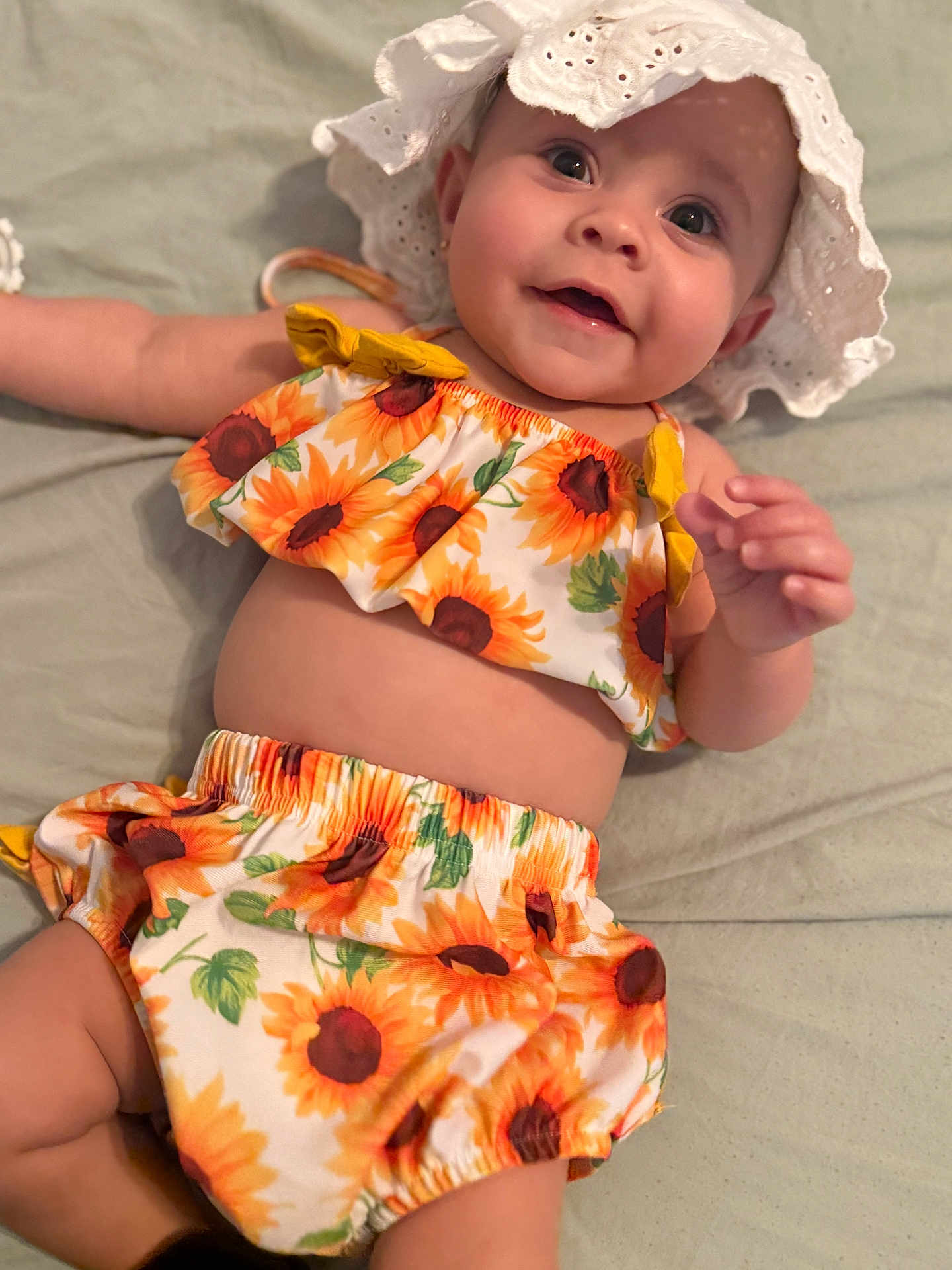 Emily Rose is registered to the contest to win money with this photo: baby, child, smiling, sunhat, sunflower, clothing, infant, cute, portrait, happy, lying_down, skin, apparel, toddler, face, hand, fabric, summer, headwear, closeup