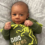 Bryson joined the competition — help win amazing prizes! baby, infant, child, face, hands, clothing, sweater, dinosaur, text, bed, blanket, pattern, lying_down, portrait, cute, smiling, skin, head, young, indoors