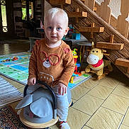 Aaron a rejoint le concours — aidez-le/la à gagner de superbes lots ! toddler, child, indoor, toy, ride_on_toy, plush_toy, rocking_horse, sweater, floor, carpet, stairs, wood, face, blue_eyes, playroom, window, door, sock, person, furniture