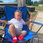 Kairi is registered to the contest to win money with this photo: blue_chair, casual_clothing, child, curly_hair, daytime, deck, expression, fence, grass, gravel_path, outdoor, person, red_socks, shorts, sitting, sunny, trees, vehicle, white_tshirt, wooden_deck