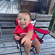 Kairi joined the competition — help win amazing prizes! toddler, child, smiling, red_shirt, chair, folding_chair, wooden_deck, outdoor, umbrella, happy, baby, socks, person, seat, wood, hand, face, grass, balcony, railing