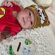 Manuel is registered to the contest to win money with this photo: baby, infant, red_clothing, brown_hat, cartoon_face, fluffy_blanket, cute, sleepy, milestone, one_month, elephant_illustration, soft_texture, portrait, child, lying_down, indoors, close_up, headwear, adorable, newborn