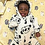 baby, child, infant, panda_onesie, hooded_clothing, smiling, tongue_out, blanket, yellow_blanket, cute, happy, lying_down, soft_texture, animal_print, black_and_white, cozy, playful, indoors, portrait, young_child