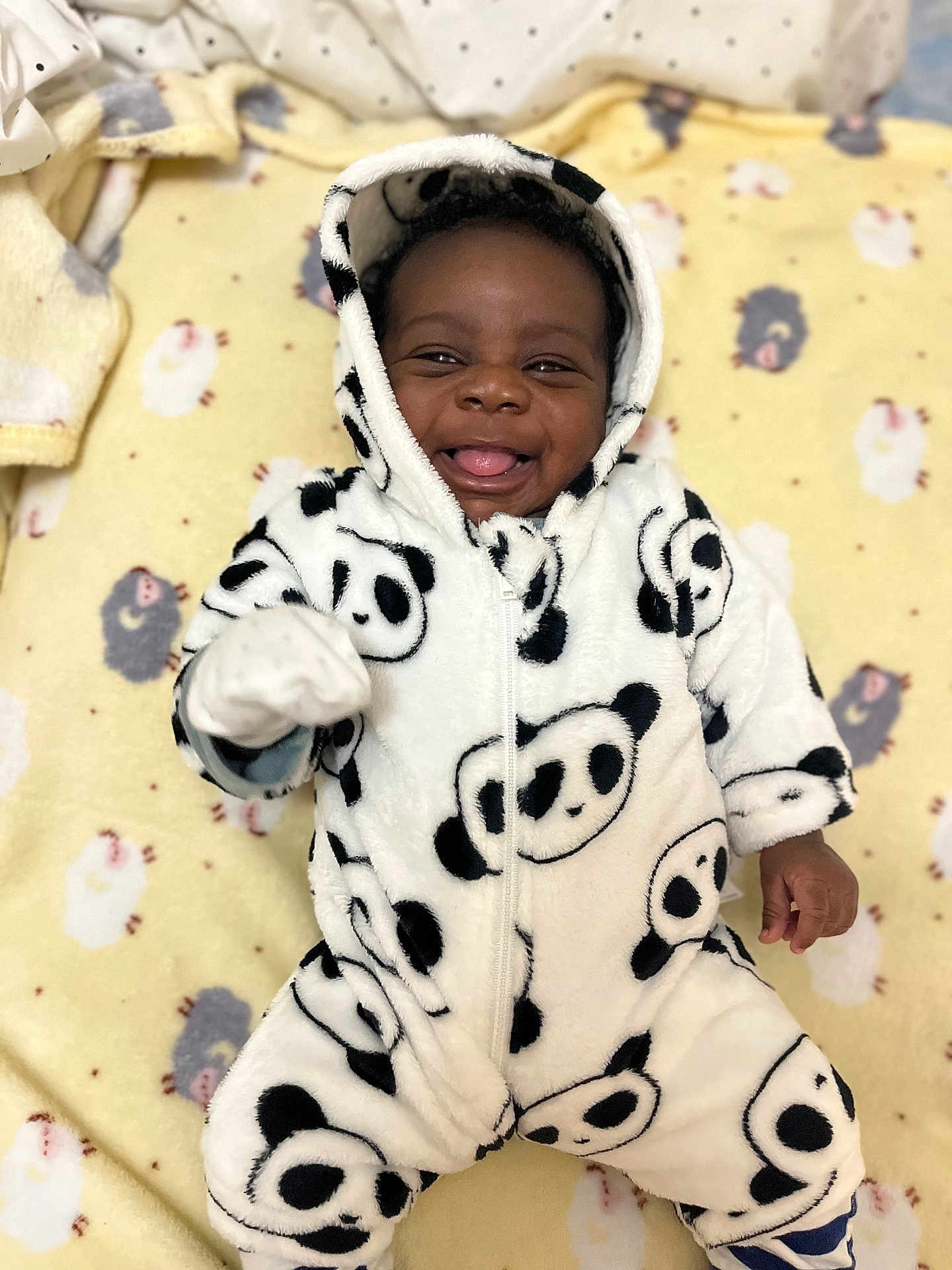 Leo is registered to the contest to win money with this photo: baby, child, infant, panda_onesie, hooded_clothing, smiling, tongue_out, blanket, yellow_blanket, cute, happy, lying_down, soft_texture, animal_print, black_and_white, cozy, playful, indoors, portrait, young_child