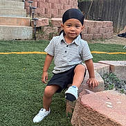 Benjamin joined the competition — help win amazing prizes! child, toddler, portrait, sitting, outdoor, garden, artificial_grass, brick_wall, retaining_wall, steps, lanterns, fence, recycling_bins, short_hair, headwear, shirt, shorts, sneakers, smiling, daylight