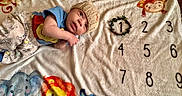 Josiah joined the competition — help win amazing prizes! animal_print, baby, blanket, child, clothing, colorful, cute, elephant, indoors, infant, knitted_hat, lion, lying_down, milestone, monkey, numbers, portrait, smiling, soft_texture, wreath