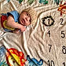baby, infant, knitted_hat, blanket, animal_print, elephant, lion, monkey, numbers, milestone, wreath, cute, lying_down, child, smiling, colorful, soft_texture, indoors, clothing, portrait