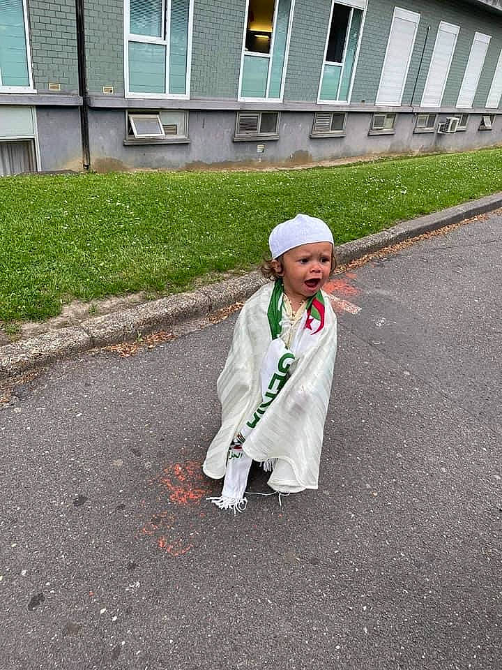 Adil participe au concours pour gagner de l'argent avec cette photo : asphalt, building, concrete, footwear, grass, hat, headgear, headwear, pedestrian, person, recreation, road, road_surface, shadow, sidewalk, sleeve, street, street_fashion, surprise, tar