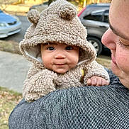 True is registered to the contest to win money with this photo: baby, child, person, hoodie, fuzzy_clothing, outdoor, car, shoulder, face, cute, expression, holding, smile, warm_clothing, tree, blurred_background, daylight, skin, young_child, parent