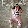 baby, bed, cartoon_print, child, cozy, cute, face, indoors, infant, pajamas, person, pink_clothing, portrait, relaxed, resting, sleeping, socks, soft_lighting, white_bedspread, young_child
