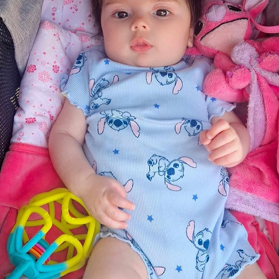 Eliya a rejoint le concours — aidez-le/la à gagner de superbes lots ! baby, blue, child, chubby_cheeks, colorful, comfort, cute, expressionless, indoors, infant, lying_down, onesie, padded_surface, patterned_clothing, pink, playful, plush_toy, rattle, small_hands, soft_toy