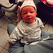 Joy a rejoint le concours — aidez-le/la à gagner de superbes lots ! baby, newborn, hat, onesie, stroller, lap, hand, tile_floor, red_bowl, bowl, indoor, person_holding, cute, portrait, seated, cozy, soft_clothing, expression, household, parent_lap