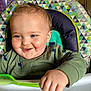 baby, child, high_chair, spoon, green_shirt, dinosaur_print, smile, face, hand, food, kitchen, indoor, person, toddler, cute, happy, messy, feeding, seat, portrait