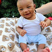 Kyàire joined the competition — help win amazing prizes! baby, smiling, blanket, teddy_bear_pattern, christmas_tree, ornaments, greenery, infant, cute, happy, white_shirt, blue_pants, toes, hand, face, outdoor, festive, holiday, person, sitting