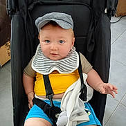 Kayden a rejoint le concours — aidez-le/la à gagner de superbes lots ! baby, child, stroller, cap, bib, blue_eyes, yellow_shirt, blue_shorts, plush_toy, elephant_toy, indoor, floor_tiles, baby_seat, cute, person, infant, clothing, seat_belt, hand, face