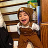 beanie, brown_overalls, cabinet, casual, child, clothing, cute, footwear, happy, indoor, laughing, person, playful, smiling, stairs, toddler, toy_bucket, white_shirt, wood_floor, wooden_stairs