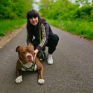 Tyson a rejoint le concours — aidez-le/la à gagner de superbes lots ! woman, dog, path, greenery, outdoor, nature, pet, animal, leash, harness, casual_clothing, sneakers, smiling, crouching, friendship, daylight, asphalt, trees, leaves, walking